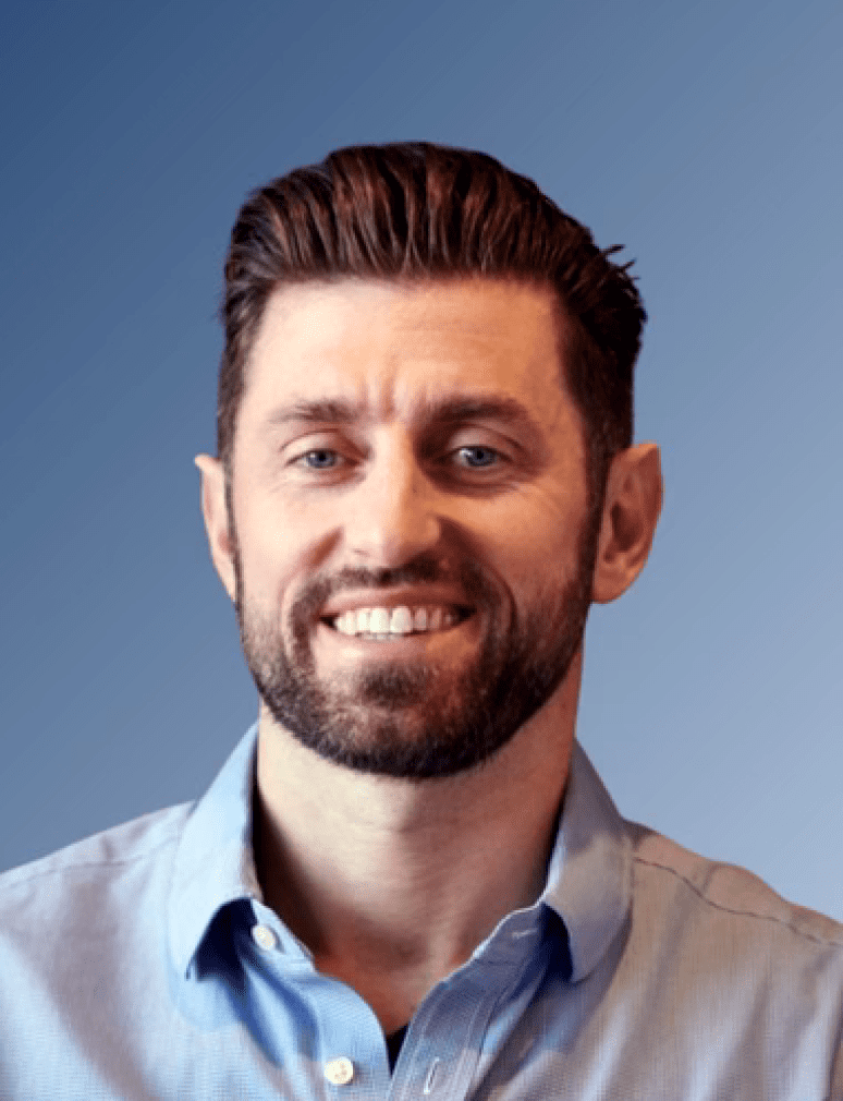 A smiling man with short brown hair and a beard, wearing a light blue shirt, poses against a blue gradient background.